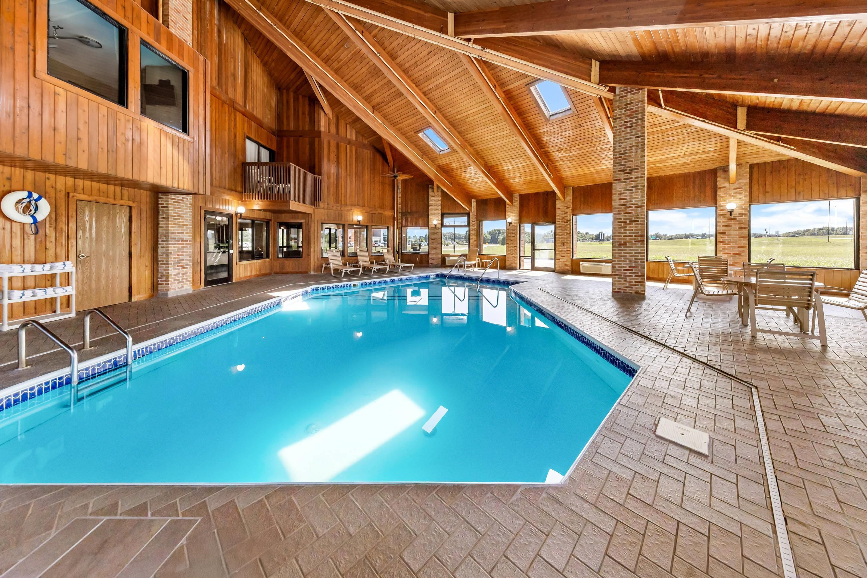 A large indoor swimming pool with a wooden interior, multiple windows, and a view of the outdoors.