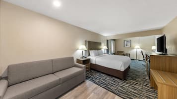 Habitación de hotel con cama, sofá, escritorio, televisión y piso alfombrado.