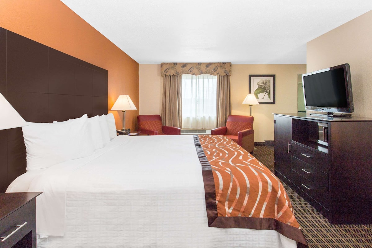 A hotel room with a large bed, two armchairs, a TV, and a dresser.