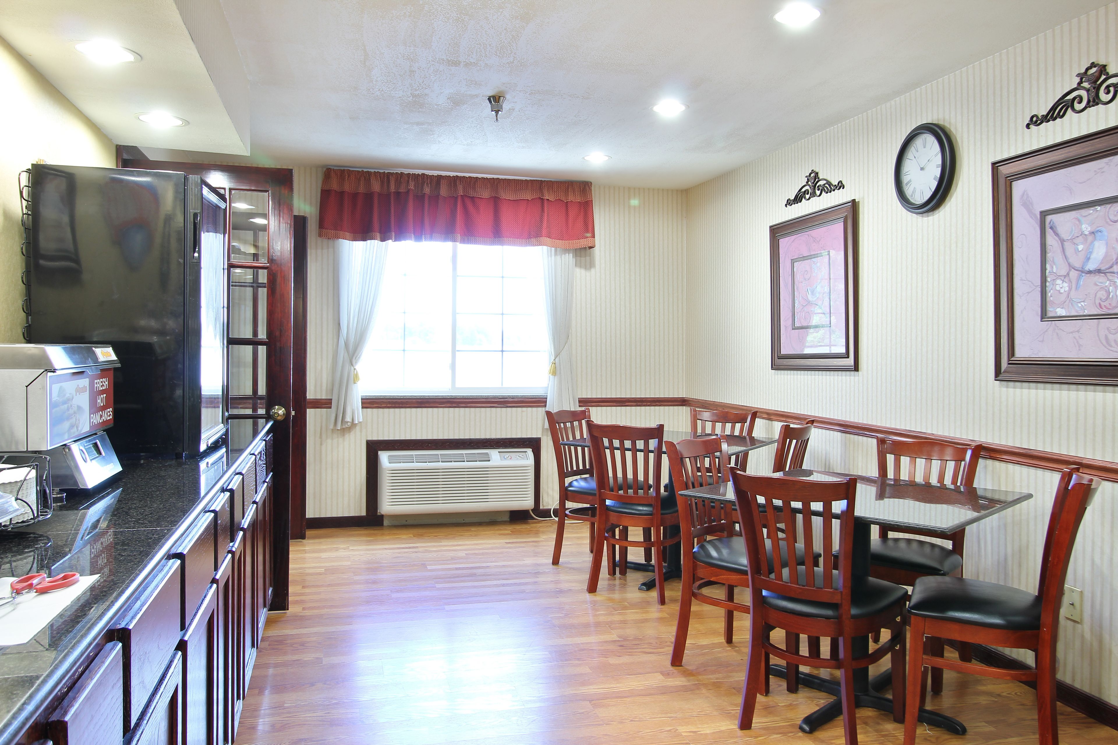 A dining area with wooden chairs and a table, a refrigerator, and a window with curtains.
