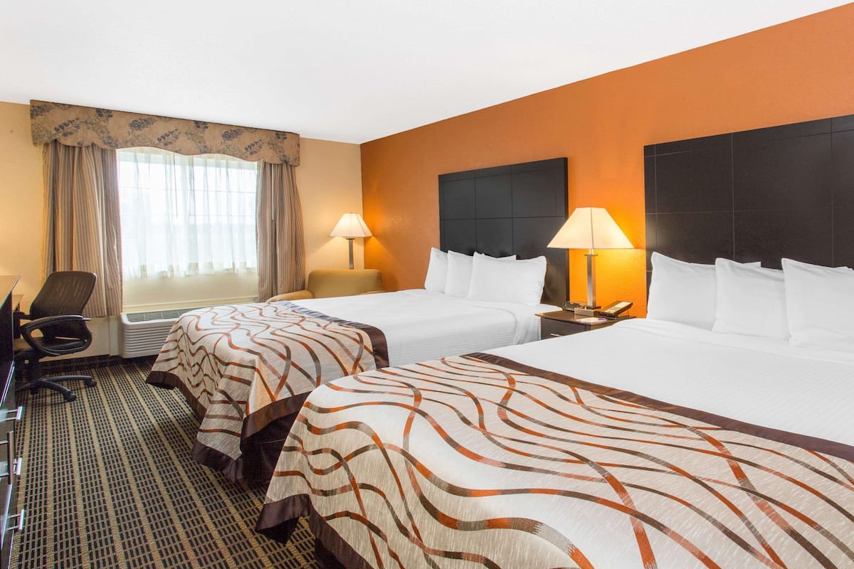 A hotel room with two beds, a desk, a chair, and a window with curtains.