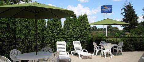 An outdoor patio with white plastic chairs and tables, green umbrellas, and a sign for Baymont Inn & Suites.