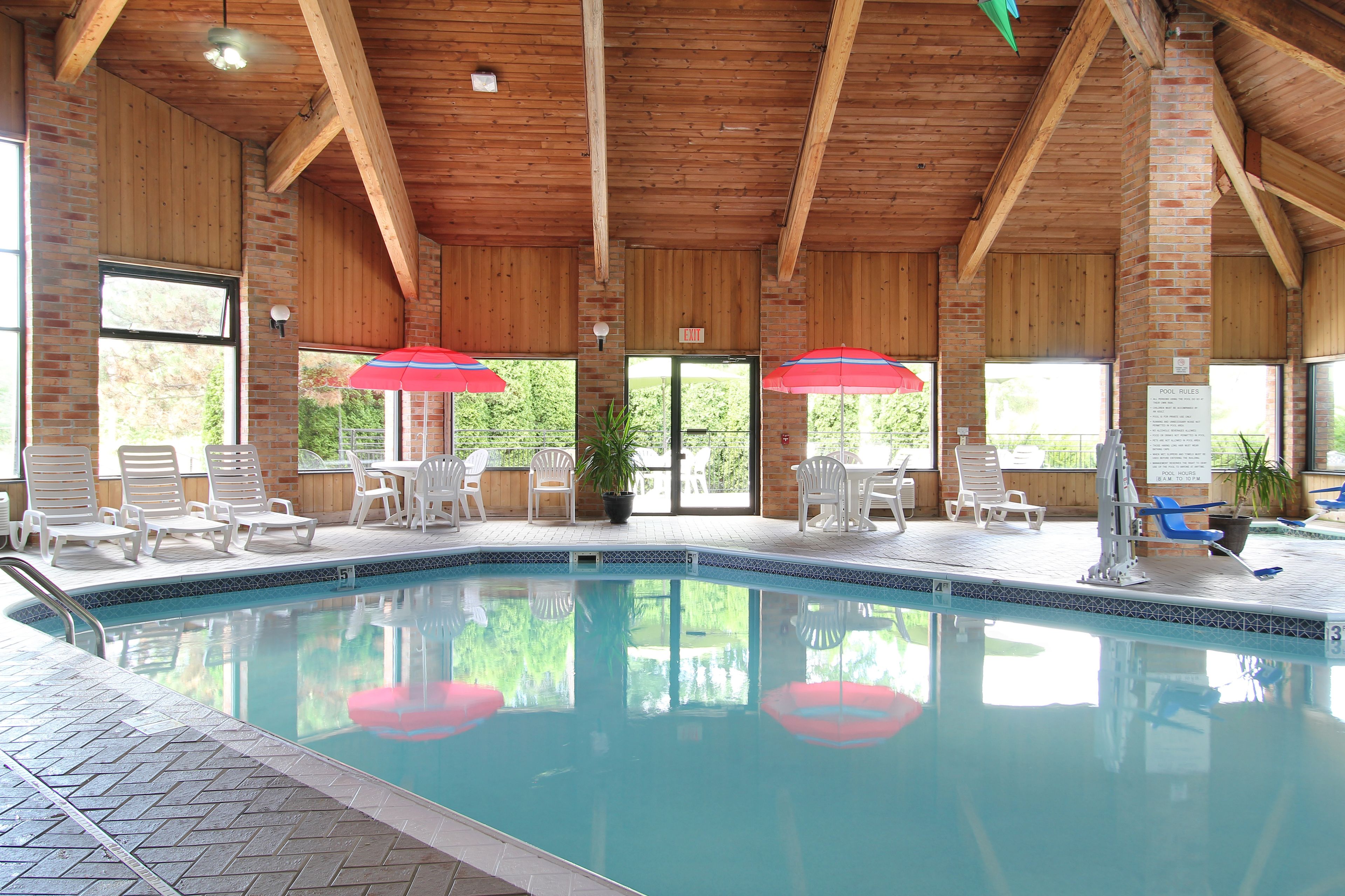 Ein Hallenbad mit Holzbalken, großen Glaswänden und weißen Liegestühlen.