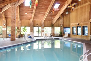 An indoor swimming pool with a wooden ceiling, clear glass windows, and a few lounge chairs. - Baymont by Wyndham Muskegon (Muskegon)