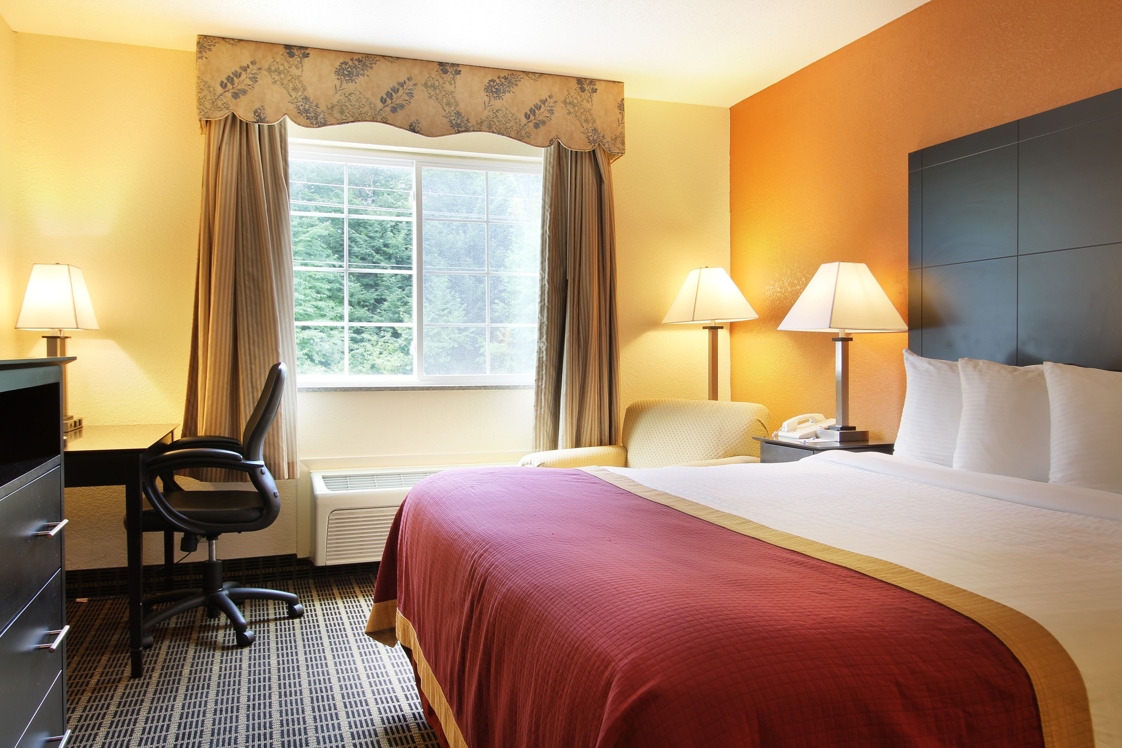 A hotel room with a bed, desk, chair, two lamps, and a telephone.