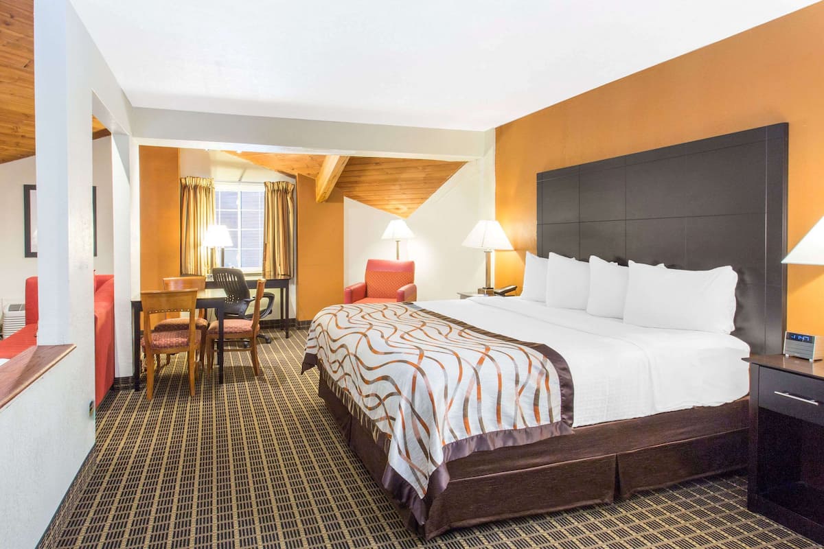 A hotel room with a large bed, a desk with a chair, two lamps, and a window with curtains.