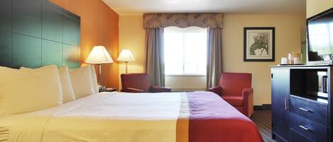 Une chambre d’hôtel avec un grand lit, deux fauteuils, un bureau avec une télévision et une fenêtre avec des rideaux.