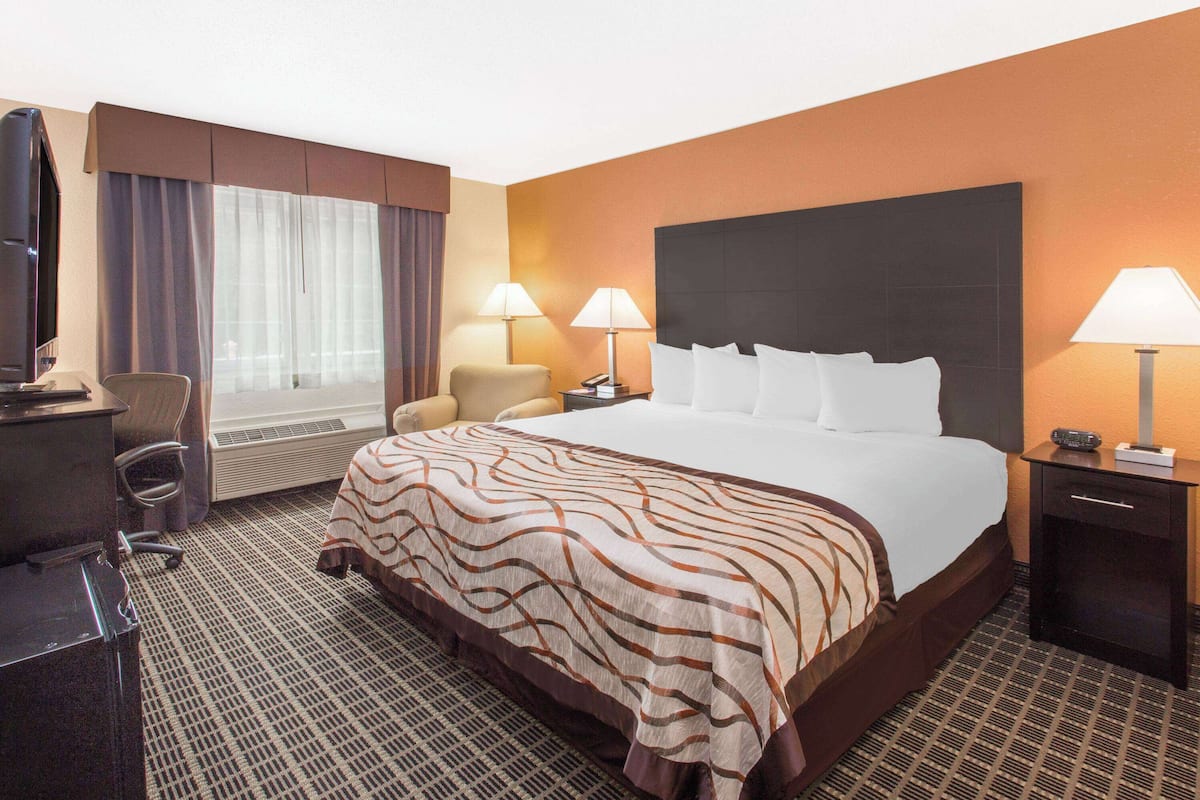 A hotel room with a large bed, two bedside lamps, a desk with a chair, a television, and a window with curtains.