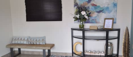 Une pièce comprenant un banc, une console sur laquelle est posé un vase de fleurs, un tableau et un objet décoratif.