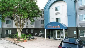 A hotel entrance with a sign for 'Sonesta Simply Suites' and a parking area with a car.
