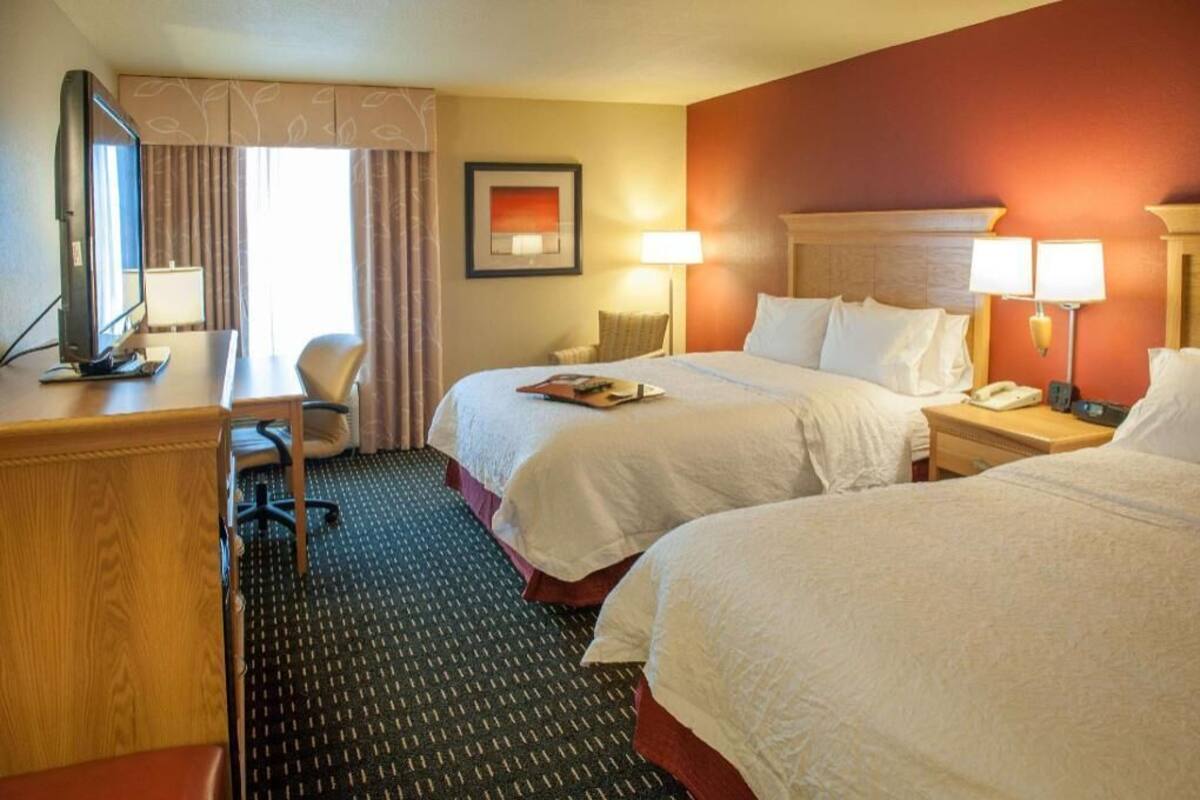 A hotel room with two beds, a desk, a chair, a television, and a window with curtains.