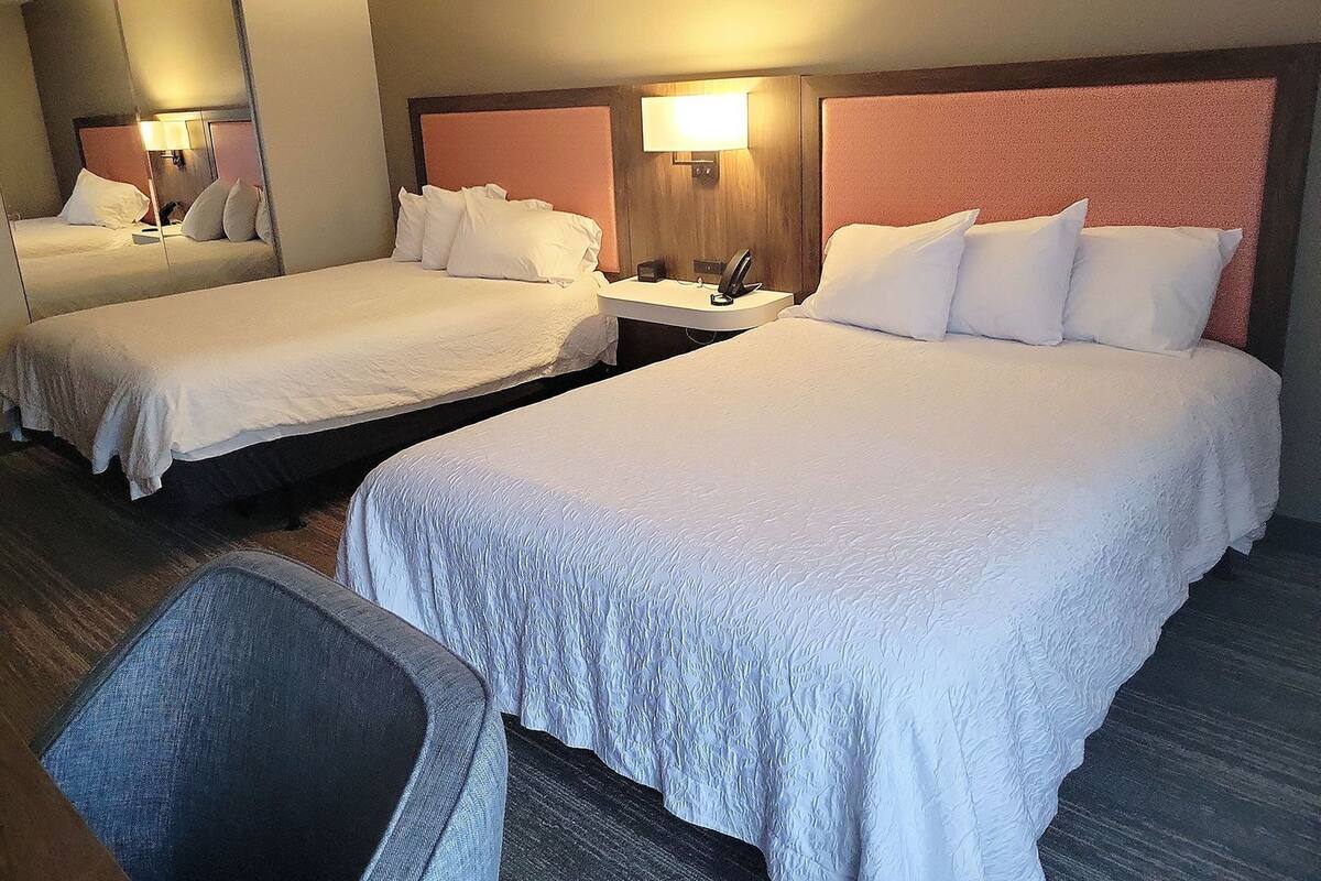 A hotel room with two beds, a desk, a chair, and a mirror.