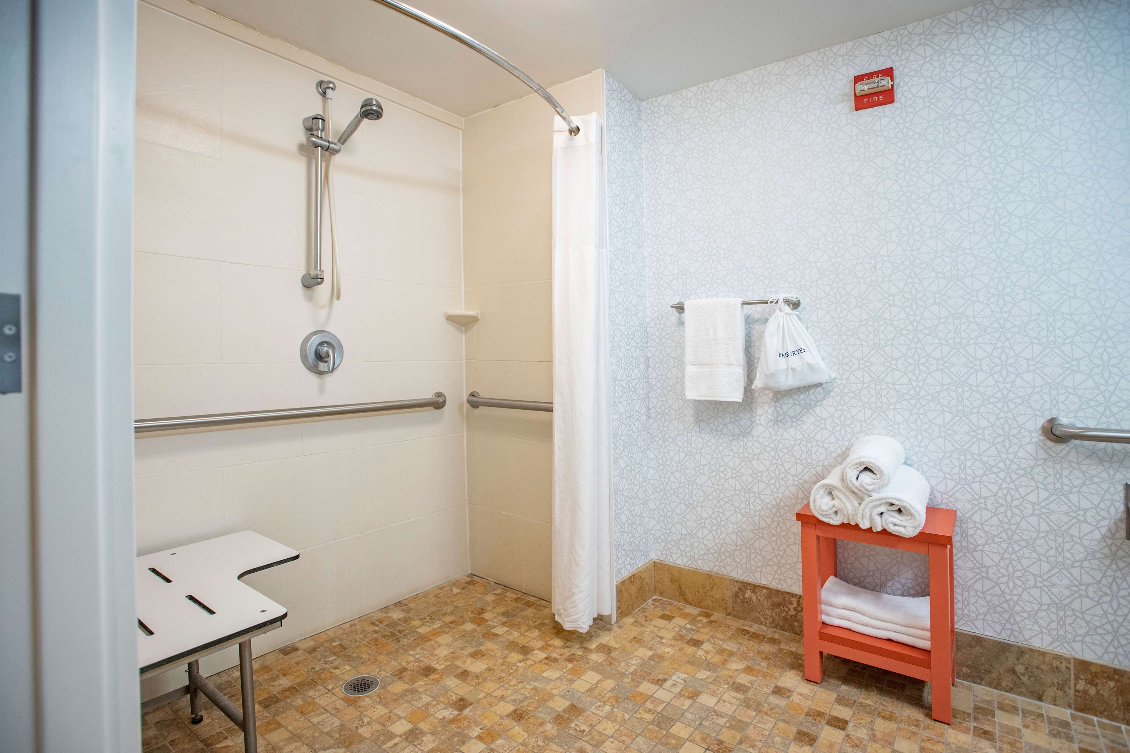 Une salle de bain équipée d’une douche, de barres d’appui, d’un porte-serviettes et d’une petite table.