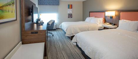 A hotel room with two beds, a desk, a chair, a TV, and a painting on the wall.