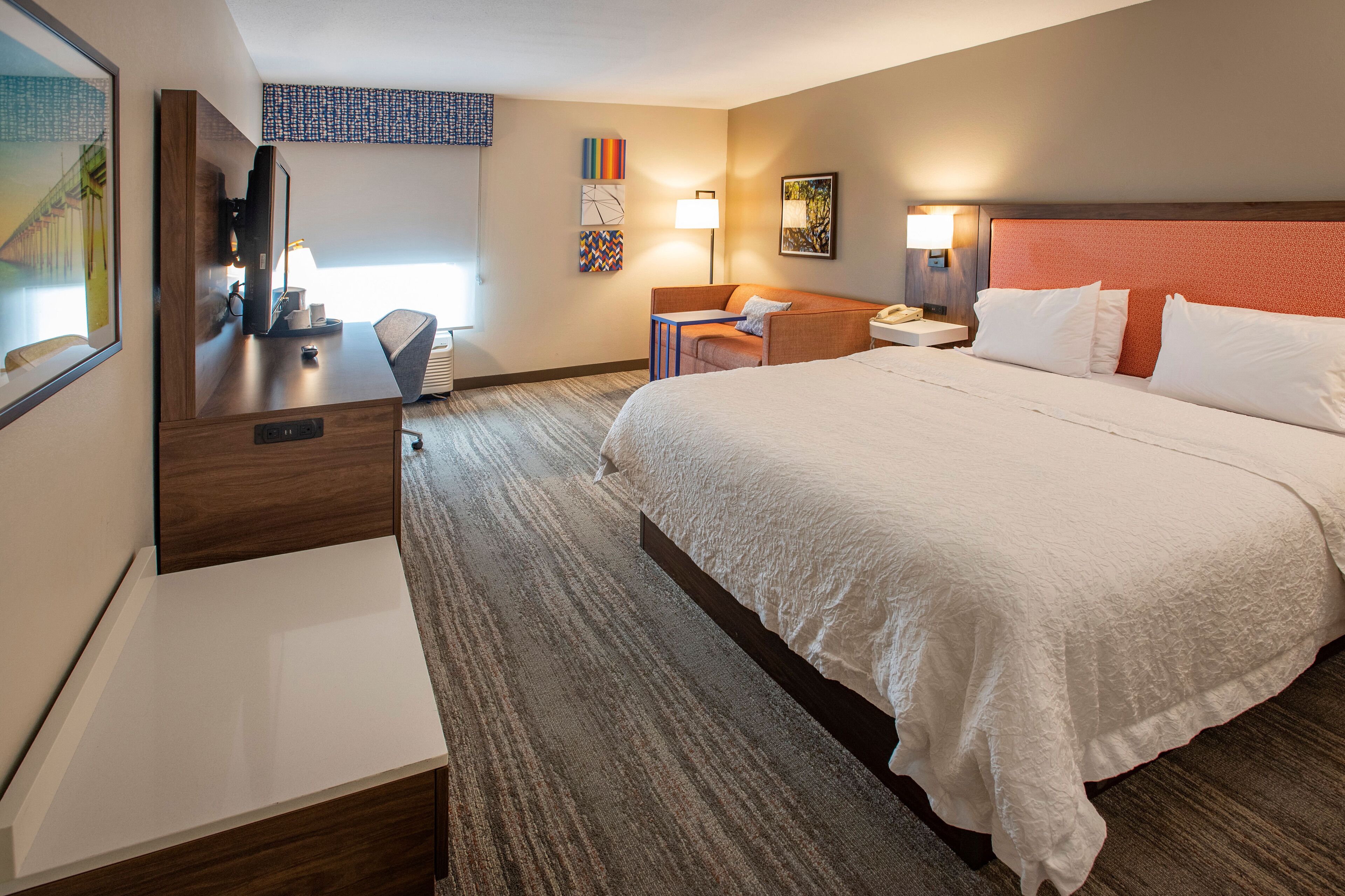 A hotel room with a large bed, a desk with a computer, a chair, and a TV.
