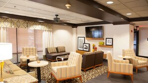 A hotel lobby with a sofa, armchairs, a coffee table, a TV, and framed pictures on the wall. - Hampton Inn Pensacola-Airport (Cordova Mall Area) (Pensacola)