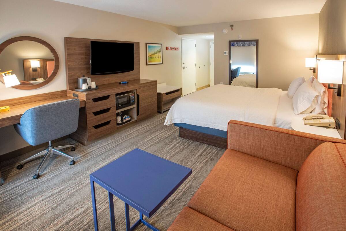 A hotel room with a bed, a desk with a computer, a television, and a small table.