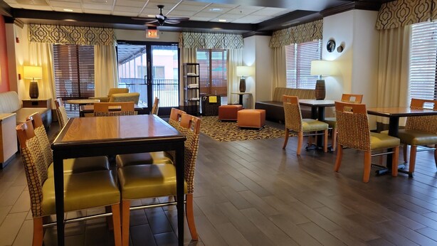 A hotel lobby with a dining area, seating arrangements, and a ceiling fan. - Hampton Inn Pensacola-Airport (Cordova Mall Area) (Pensacola)