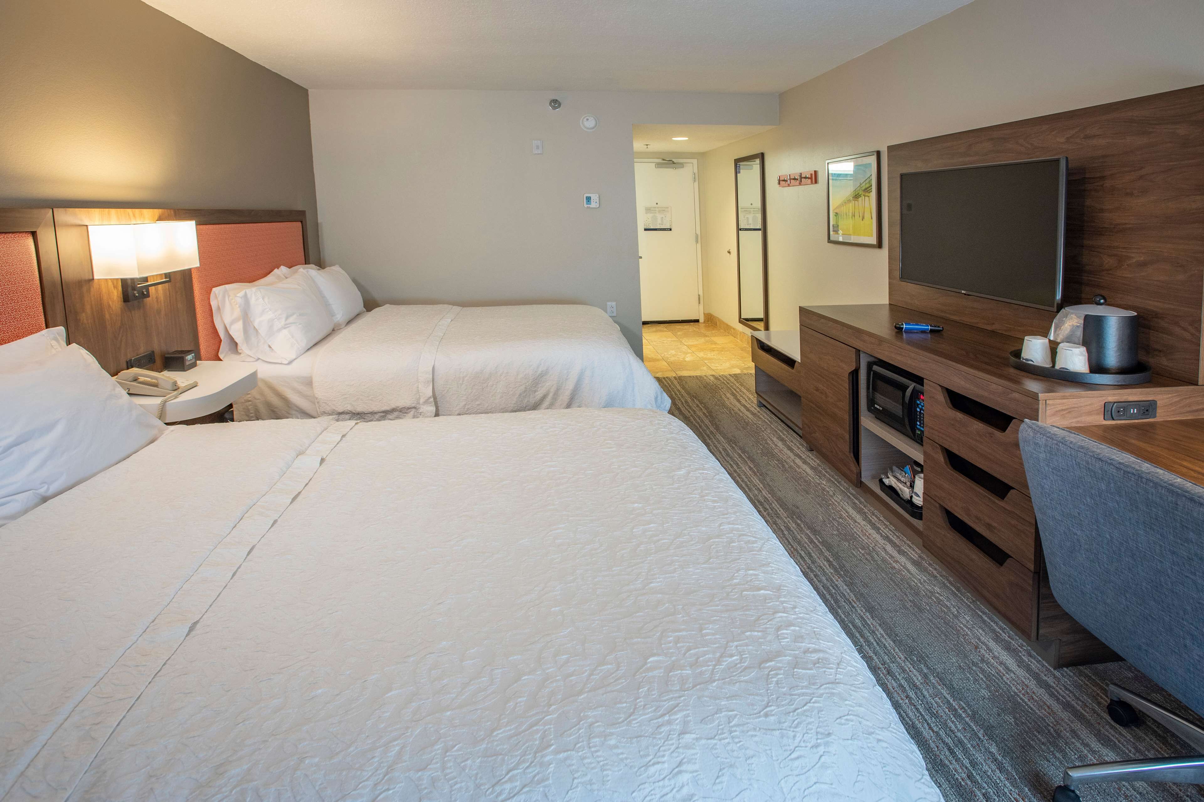 Habitación de hotel con dos camas, televisor, escritorio y espejo.