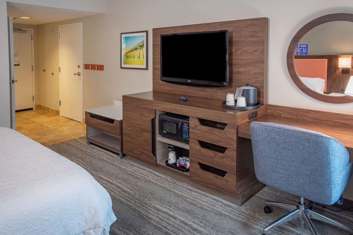 A hotel room with a bed, a desk with a television, a microwave, and a coffee maker.
