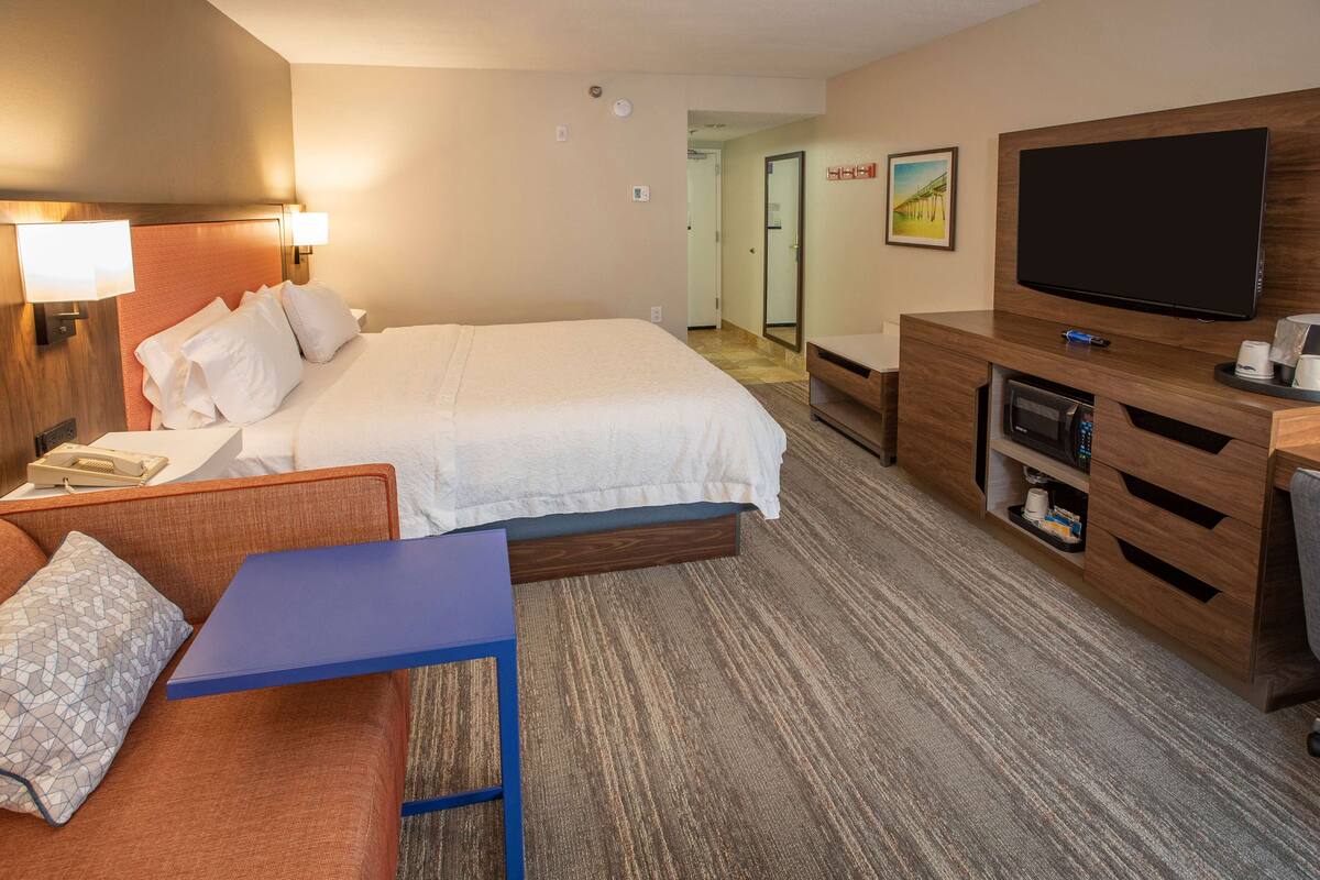 A hotel room with a bed, a desk, a television, and a mirror.