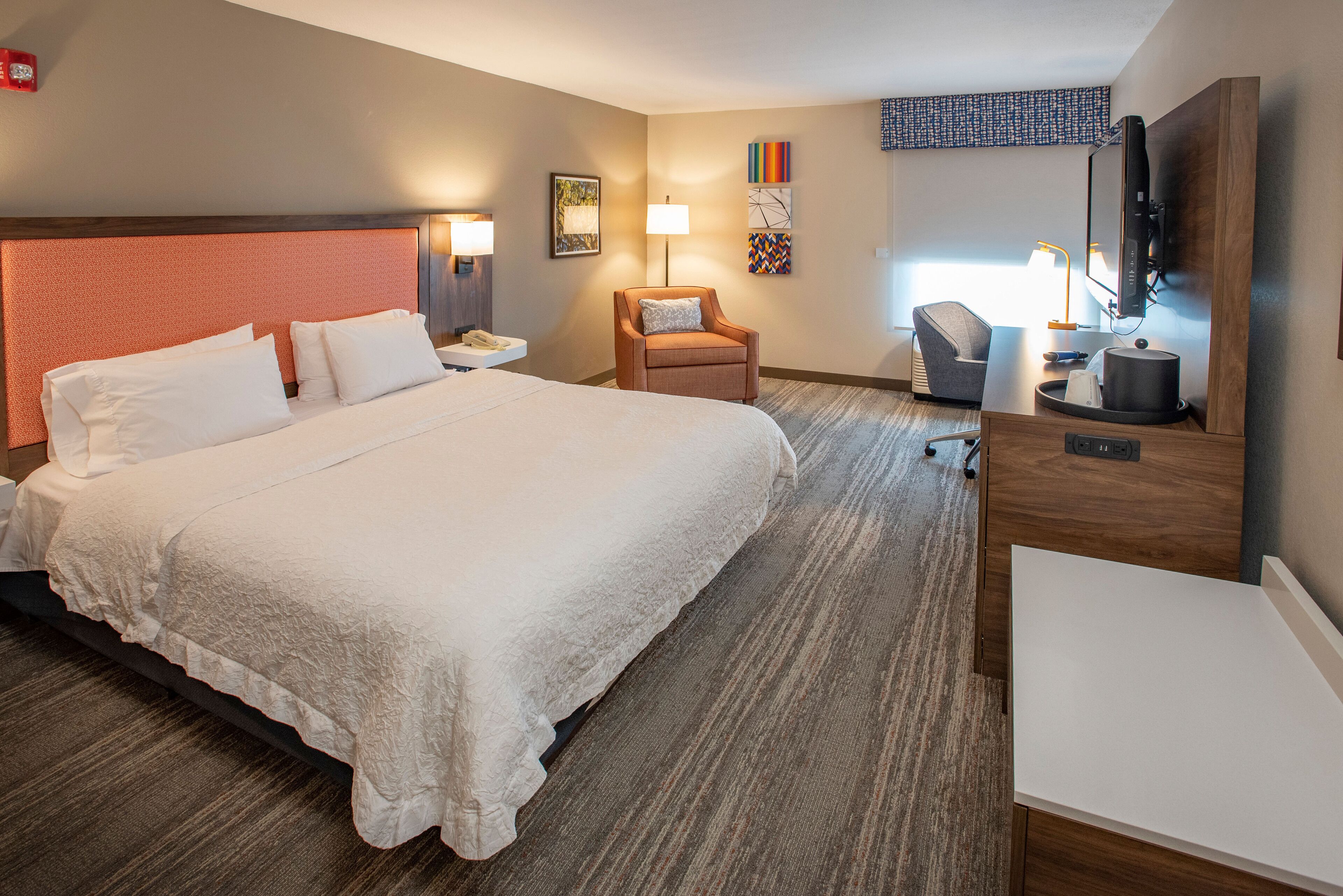 A hotel room with a large bed, a desk with a chair, a TV, and a lamp.