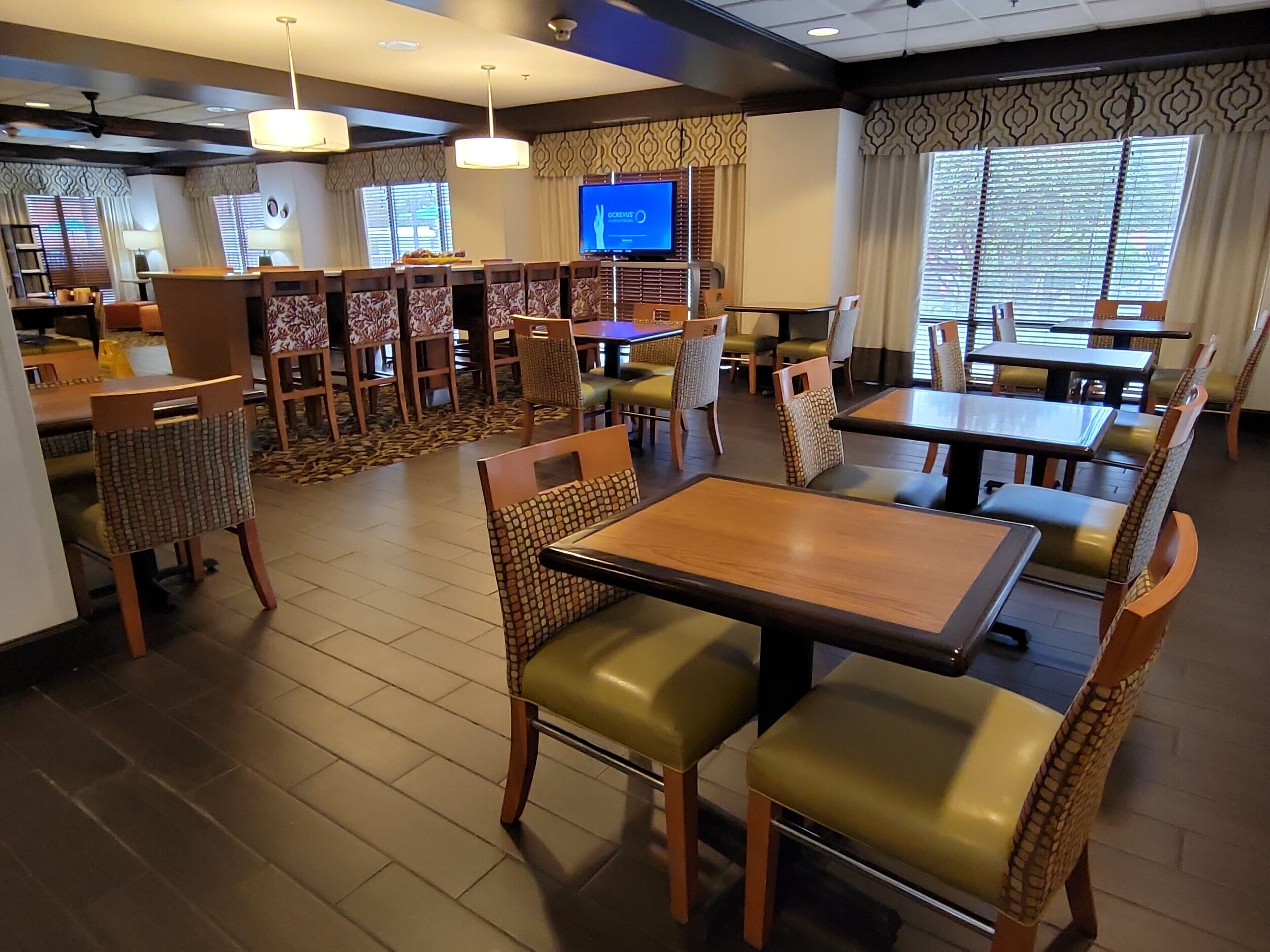 Un restaurant avec des tables et des chaises en bois, un écran de télévision et des rideaux à motifs.