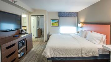 A hotel room with a bed, a TV, a desk, and a bathroom visible through an open door.
