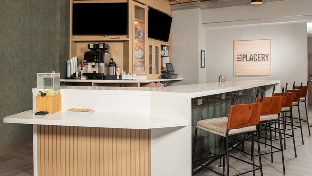 A modern bar area with a white counter, wooden accents, and bar stools. - Hyatt Place Denver South/Park Meadows (Lone Tree)