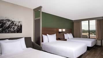 Een hotelkamer met twee bedden, een groot raam met uitzicht, een schilderij aan de wand en een houten hoofdeinde.