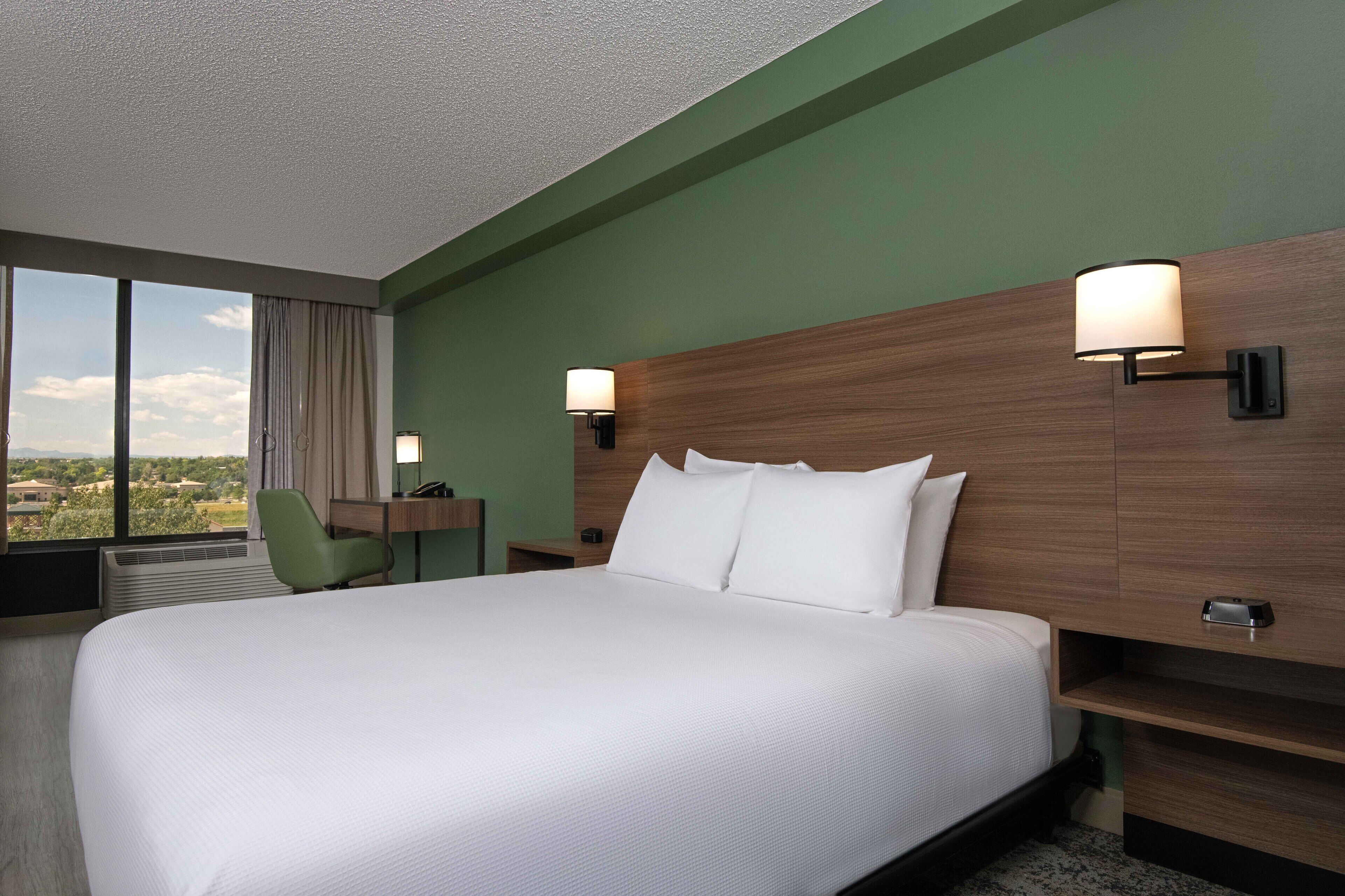 A hotel room with a large bed, a desk, a chair, and two wall-mounted lamps.