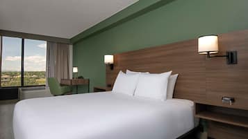 A hotel room with a large bed, a desk, a chair, and two wall-mounted lamps.