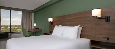 Quarto de hotel com uma cama grande, uma escrivaninha, uma cadeira e duas luminárias fixadas na parede.