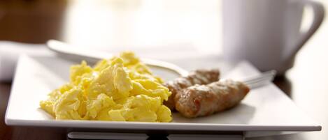 A breakfast plate with scrambled eggs and sausages on a white plate, accompanied by a white cup.