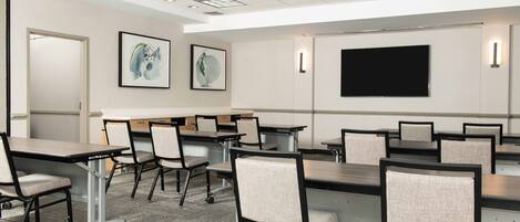 A conference room with tables and chairs, a large screen, and artwork on the walls.