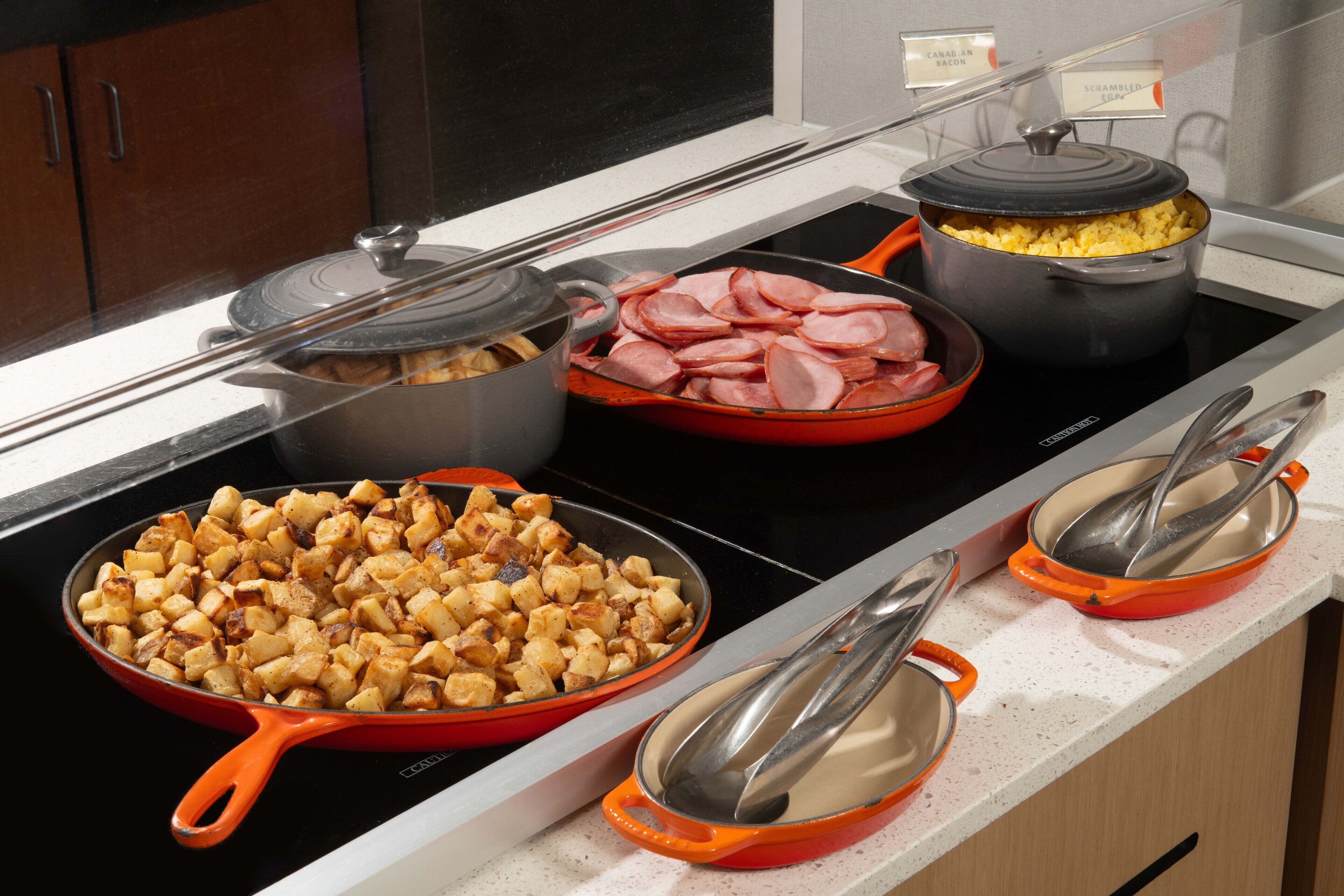 A buffet with various dishes including scrambled eggs, ham, and roasted potatoes.