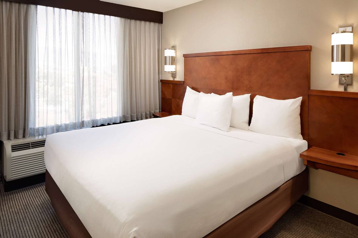 A large bed with white linens, a wooden headboard, and two bedside lamps.