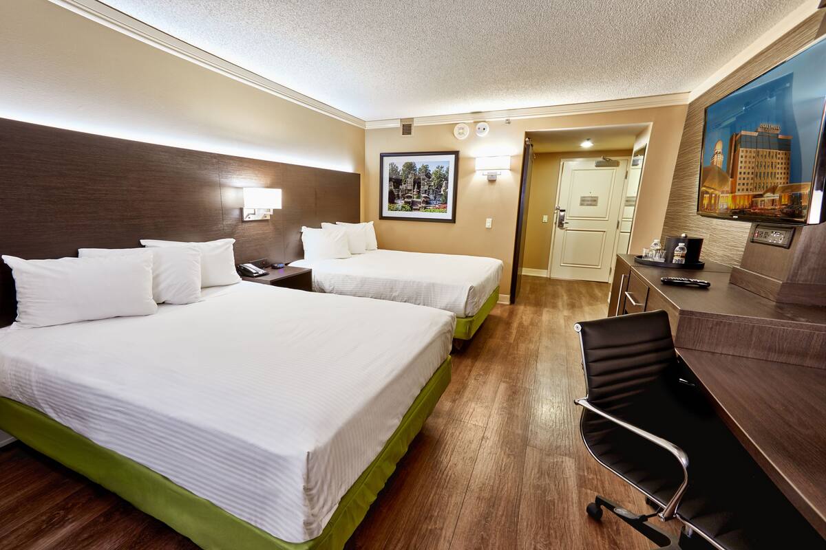 Habitación de hotel con dos camas, un escritorio, una silla, un televisor y la puerta del baño.