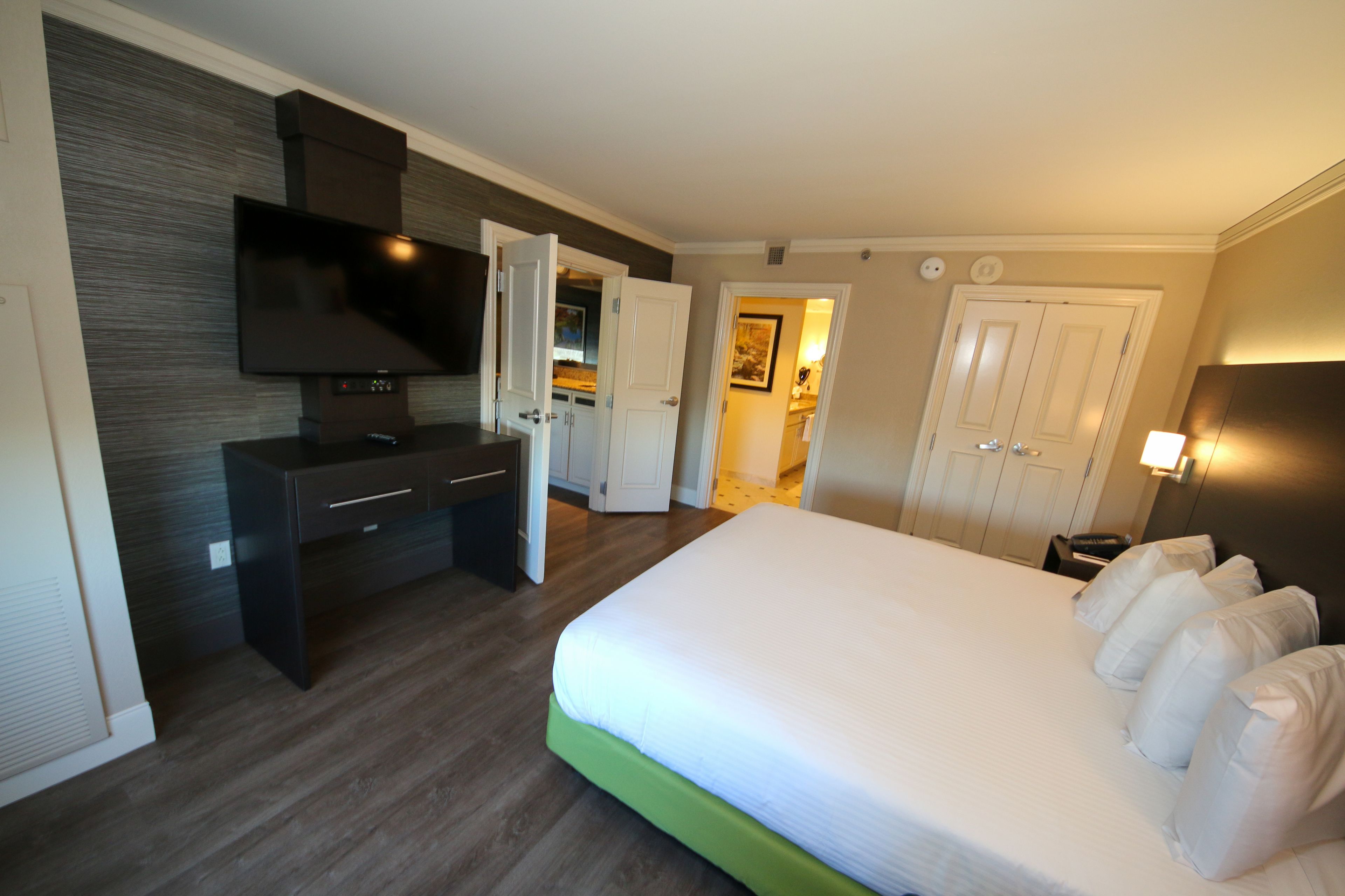 A hotel room with a bed, a TV, a desk, and a door leading to a bathroom.