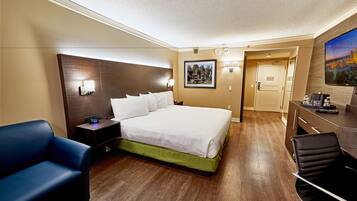 Hotelkamer met een groot bed, een bureau, een stoel, een nachtkastje, een aan de muur bevestigde televisie en een deur naar een andere kamer.