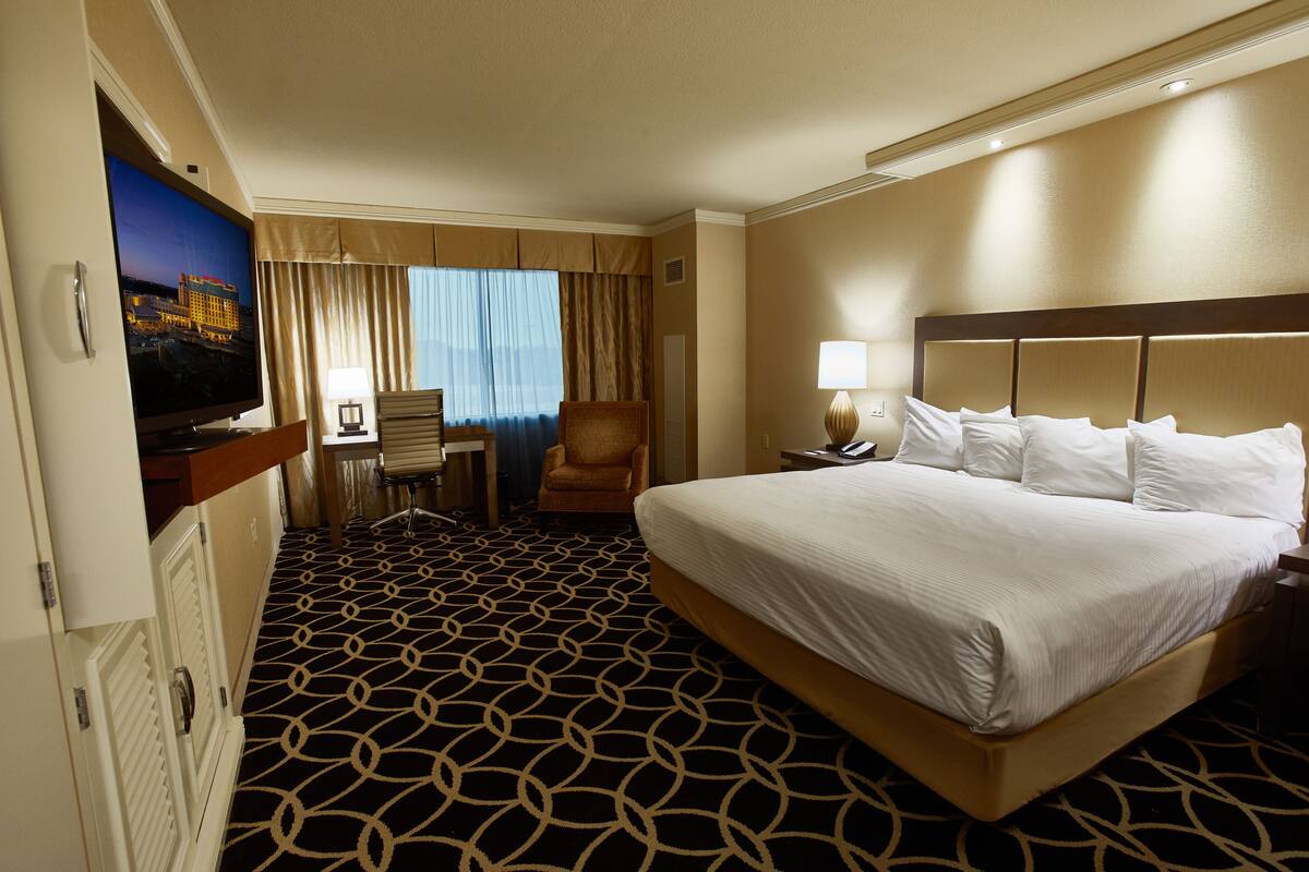 Una habitación de hotel con una cama grande, televisión, escritorio y una silla.