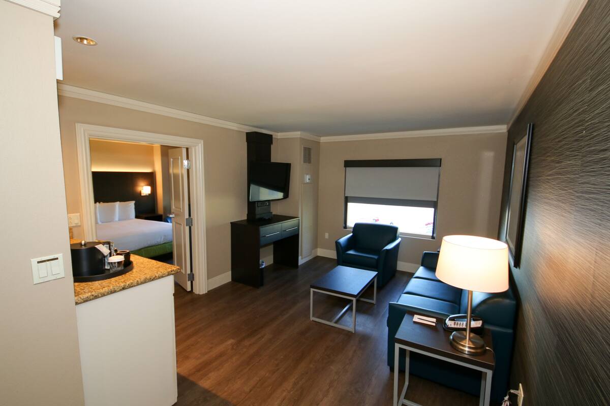 Habitación de hotel con cama, escritorio, silla y una mesita de noche con lámpara.