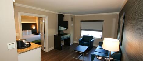 A hotel room with a bed, desk, chair, and a small table with a lamp.