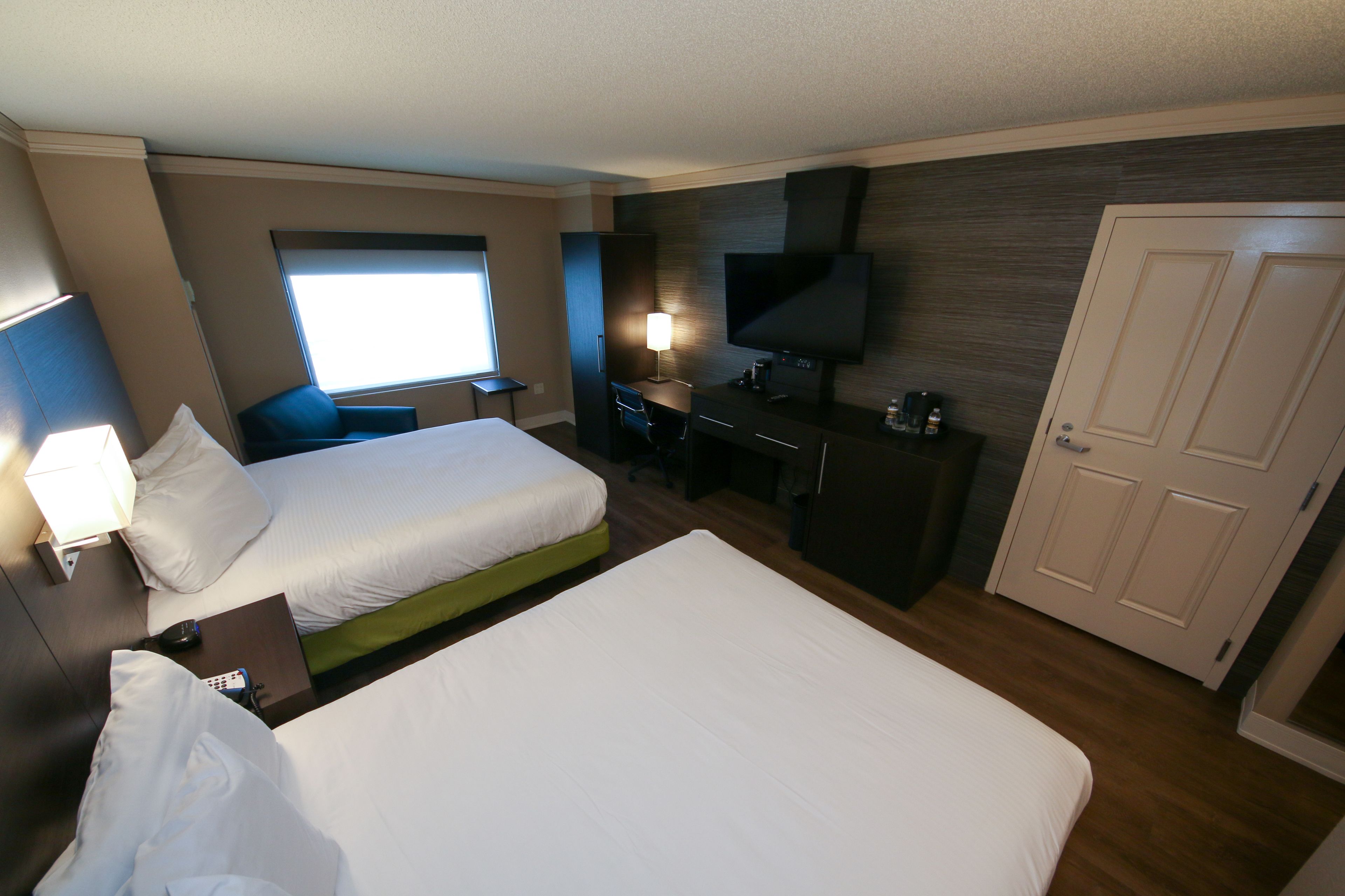 A hotel room with two beds, a desk, a TV, and a door.