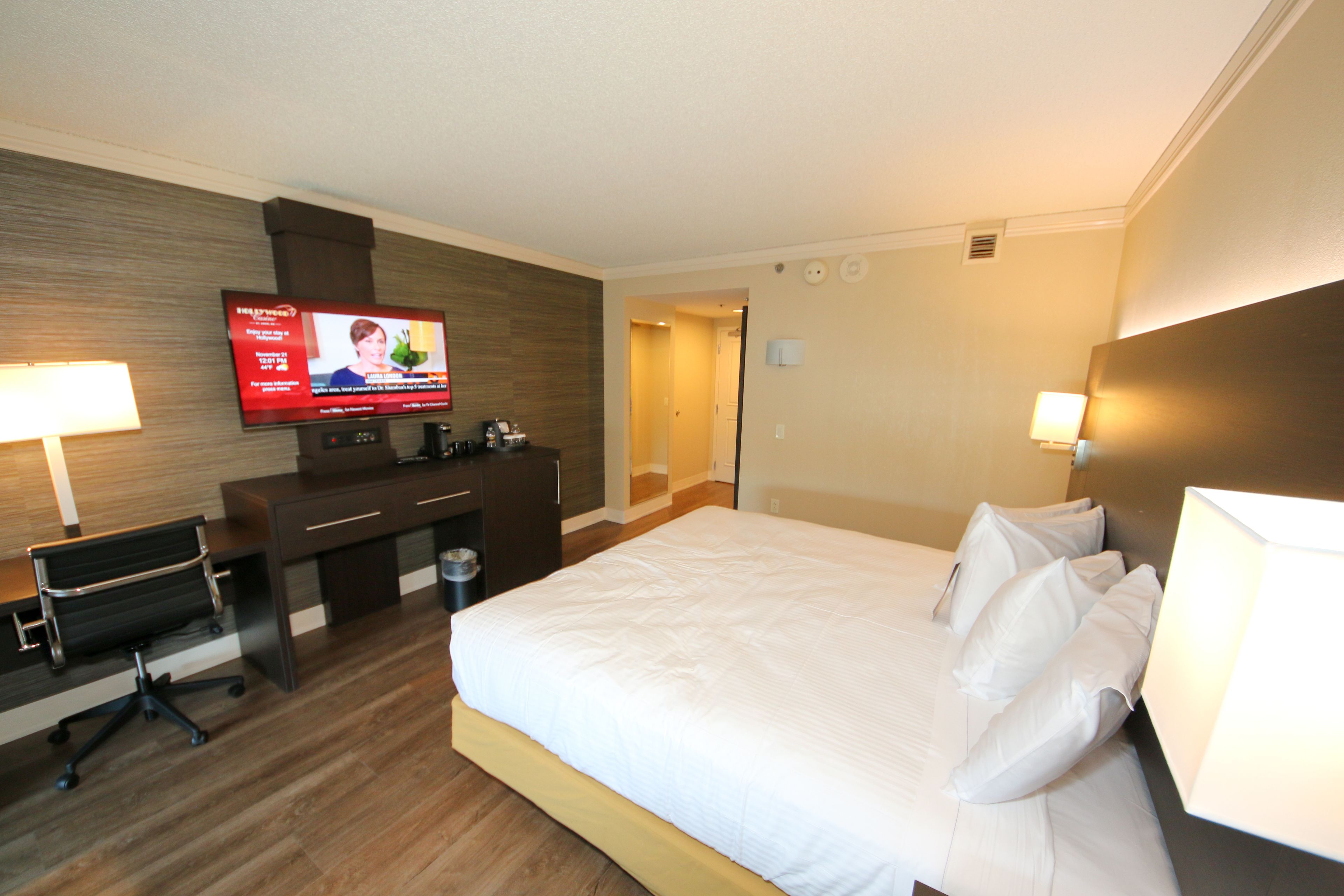 A hotel room with a large bed, a desk with a computer, a television, and two lamps.