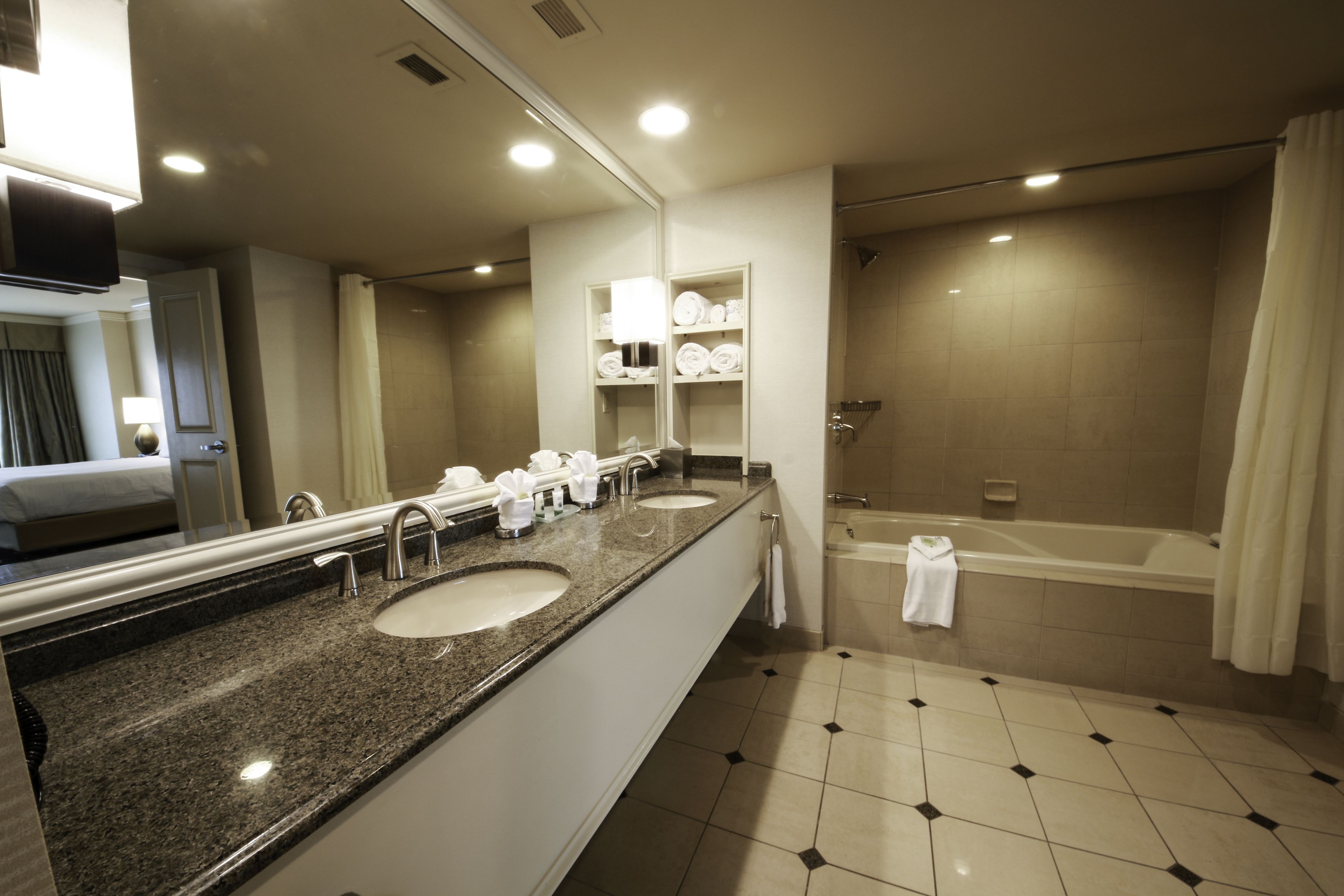Un bagno d'hotel con uno specchio grande, due lavandini, una vasca e una doccia.