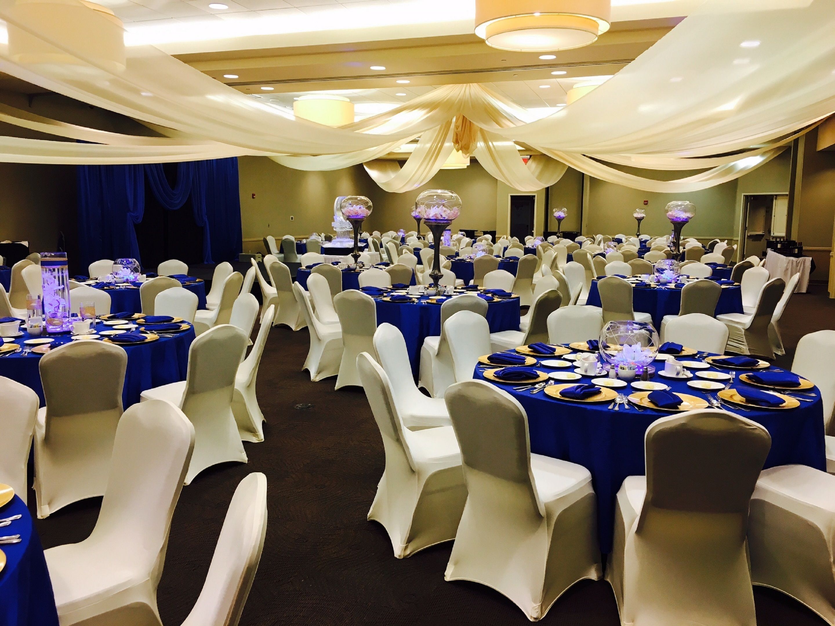 Une salle de banquet avec des tables rondes, des chaises blanches et des nappes bleues.