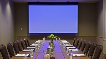 A conference room with a long table, chairs, water bottles, and a projector screen.