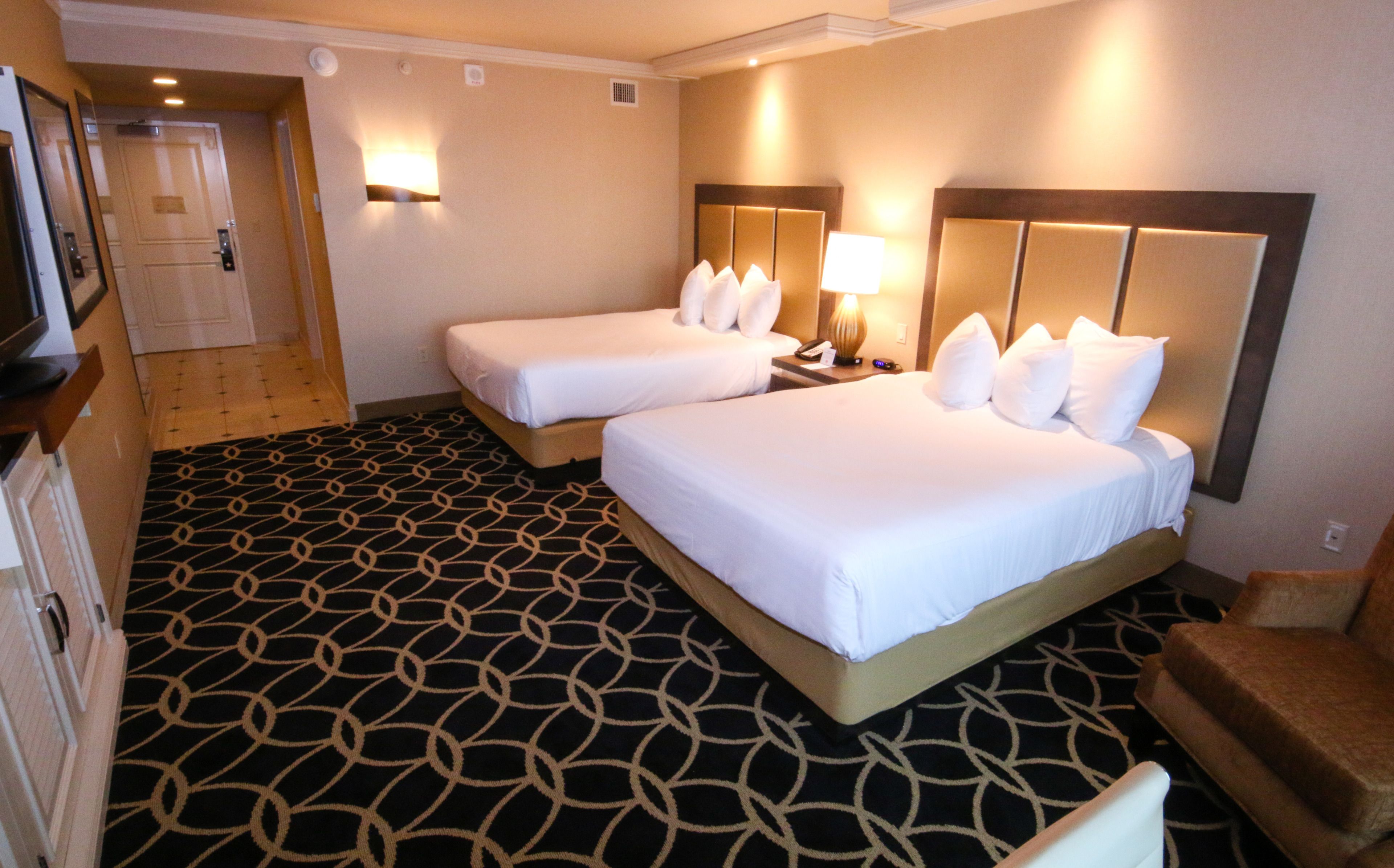 A hotel room with two beds, a patterned carpet, a wooden headboard, and a nightstand with a lamp.