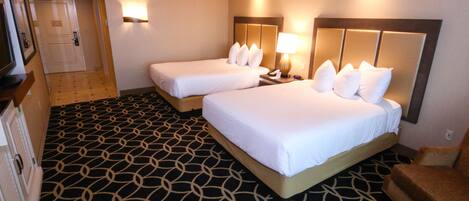 A hotel room with two beds, a patterned carpet, a wooden headboard, and a nightstand with a lamp.
